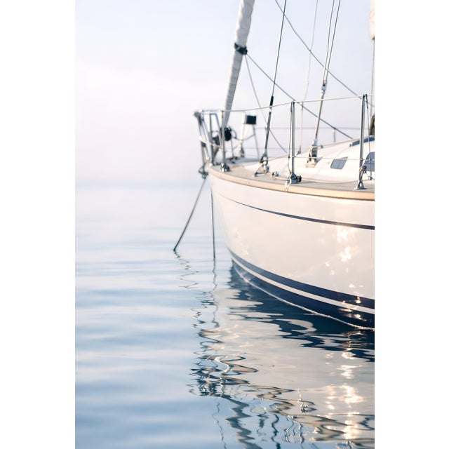 Minimalist coastal artwork featuring a sailboat resting on calm water with soft reflections and clean lines. The...