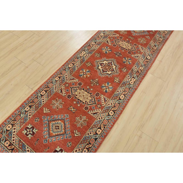 A tribal Caucasian Kazak runner hand-knotted with an all-wool pile on a cotton foundation. This oriental rug features...