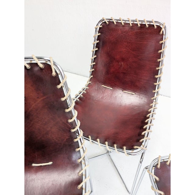 Set of four mid-century dining chairs, featuring thick brown leather sling seats laced by hand to chrome tubular frames....