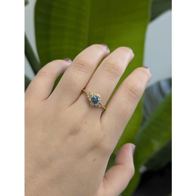 This enchanting blue diamond ring captures the delicate grace of a flower in full bloom. A 0.44 carat round blue diamond...