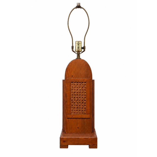 A sculptural vintage table lamp featuring a warm brown wooden body with an arched top, a framed woven cane inset, and a...