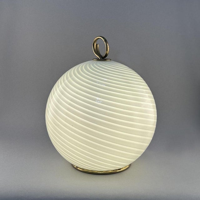 Spherical Venini glass table lamp is hand blown in white Filigrana cane work that spirals around to create extra movement....
