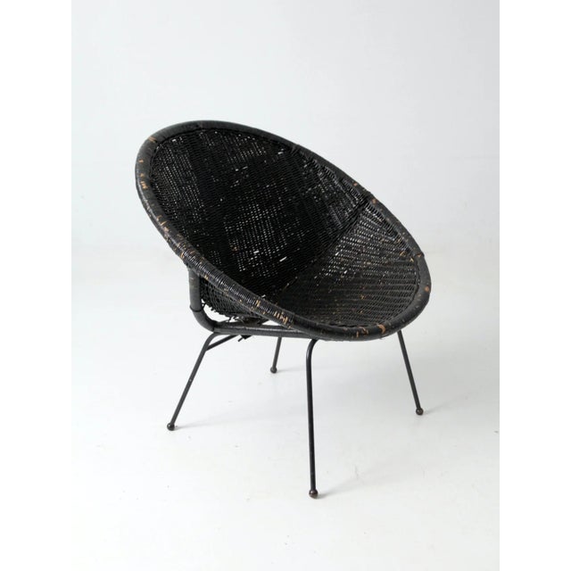 A mid-century modern black wicker saucer chair with a sleek, minimalist profile. the rounded woven seat creates bold...