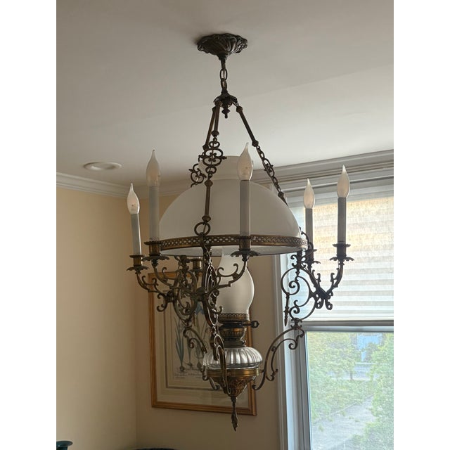 Beautiful vintage chandelier featuring an ornate cast-metal frame with intricate scrollwork and a warm antique brass...