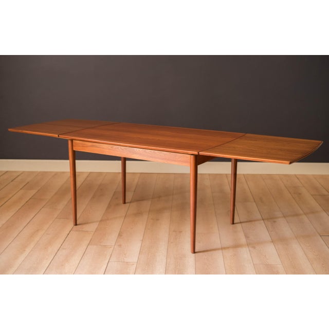 Mid Century Modern draw leaf dining table in teak, circa 1960s. This unique boat shaped tabletop features continuous...