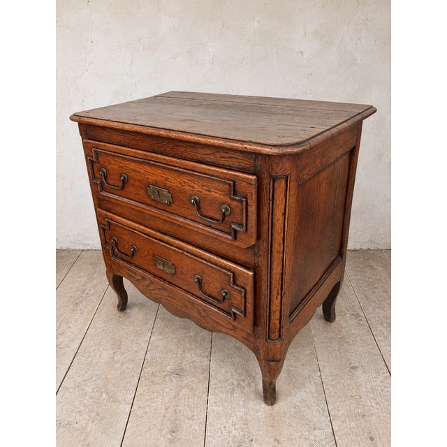An antique French country commode with rich wood grain and beautifully worn details. This chest of drawers features two...
