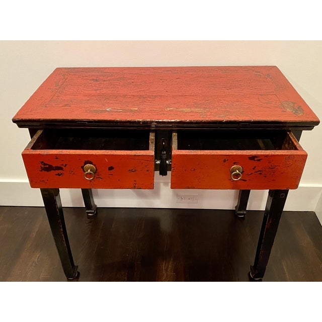 A Chinese altar table, desk or console in lacquered wood with a striking and heavily distressed finish in a red and black...