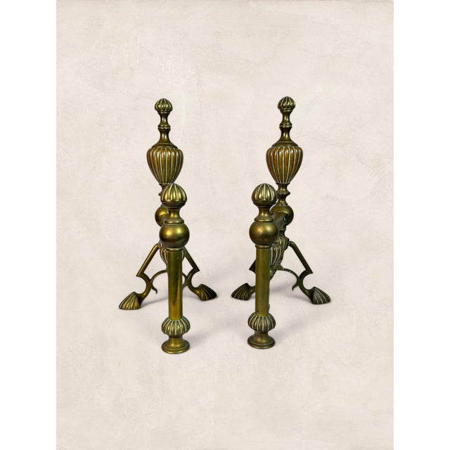 An elegant pair of antique solid brass andirons featuring beautifully fluted urn finials, turned baluster stems, and...