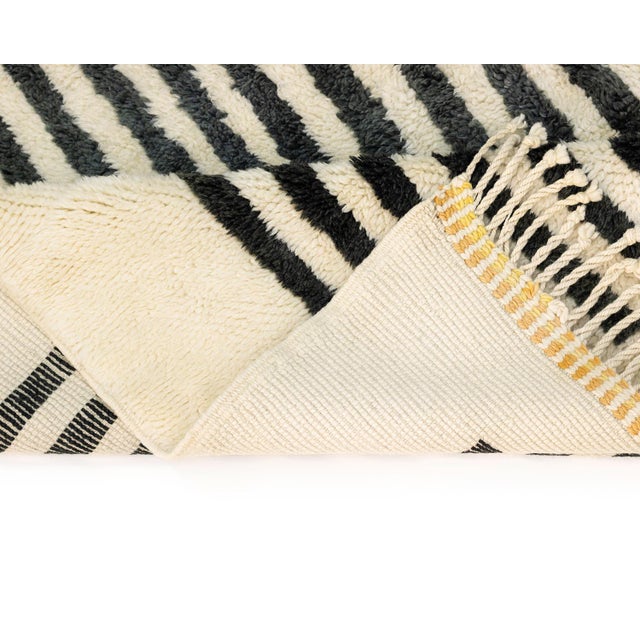 A striped curtain of black falling over a soft pastel landscape. This hand-knotted wool rug frames its composition with a...