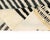 A striped curtain of black falling over a soft pastel landscape. This hand-knotted wool rug frames its composition with a...