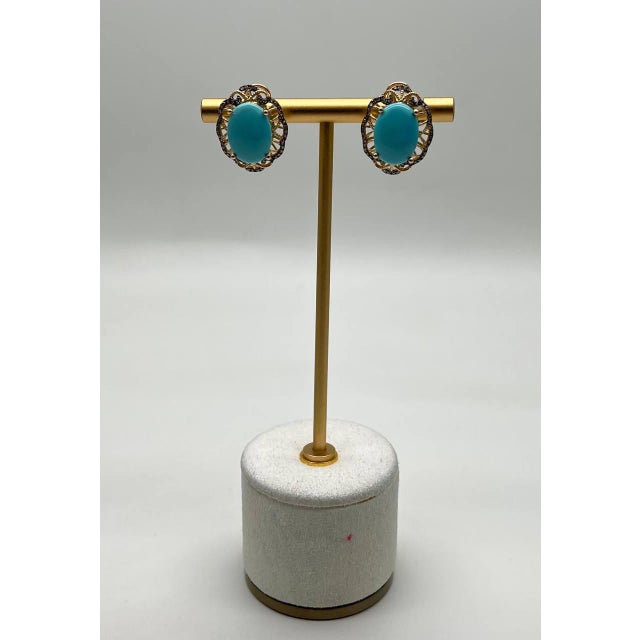 These exquisite earrings feature a vibrant turquoise oval stone set in a delicate gold frame. The intricate design...
