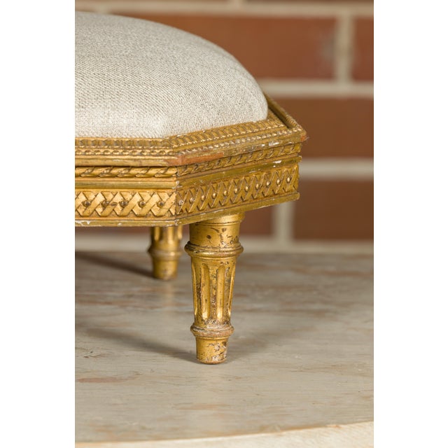 A French Neoclassical carved giltwood footstool from the 19th century with custom linen upholstery. This exquisite 19th-...