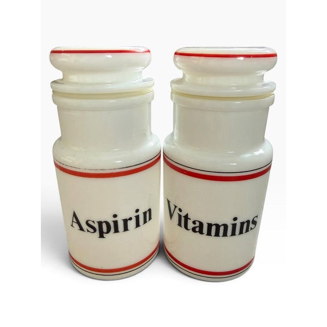 Striking vintage pair of ceramic apothecary jars labeled “Aspirin” and “Vitamins,” presented in a crisp ivory-and-red...