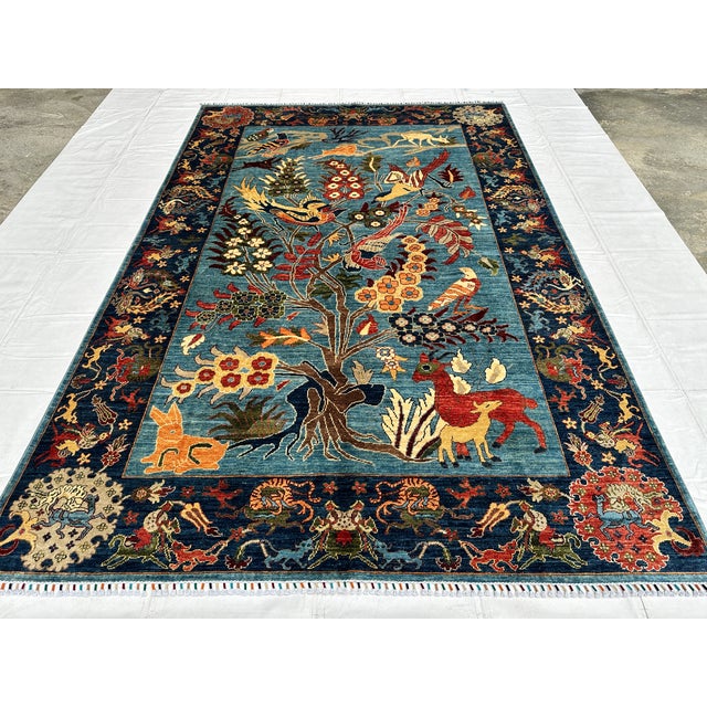 This hand-knotted Afghan pictorial rug centers a single flowering tree filled with exotic birds, surrounded by a rabbit,...