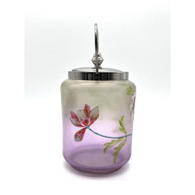 A hand-painted antique glass jar with a vibrant floral design, typical of the Art Nouveau or late Victorian period. The...