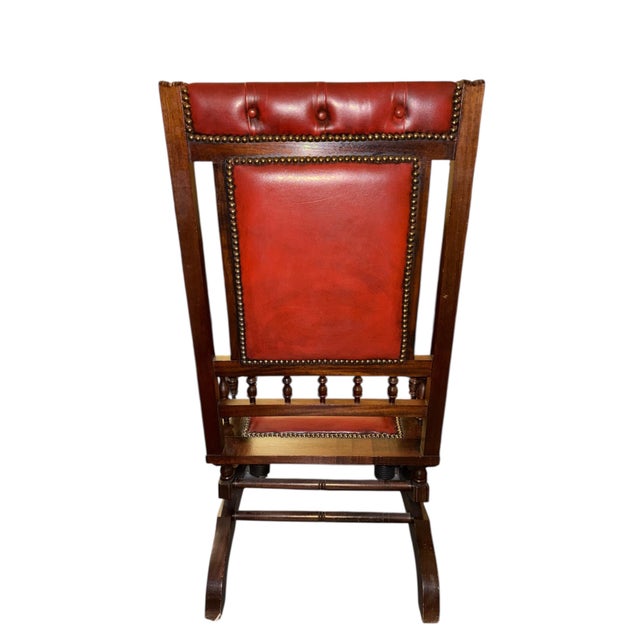 English platform rocking chair upholstered in deep button-tufted oxblood leather in the Chesterfield tradition. Solid...
