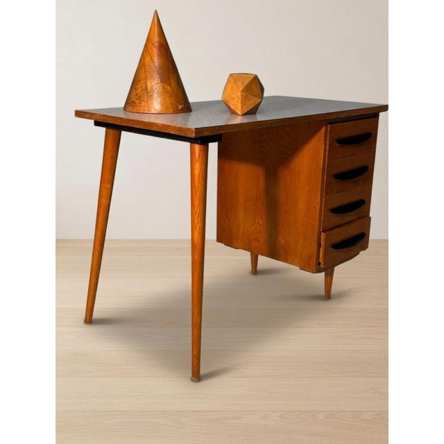 A distinctive mid-century writing desk featuring a rectangular writing surface, four integrated drawers, and slender...