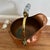 Handsome vintage copper coal scuttle featuring a rounded body, flared pouring edge, pedestal base, and brass swing handle....