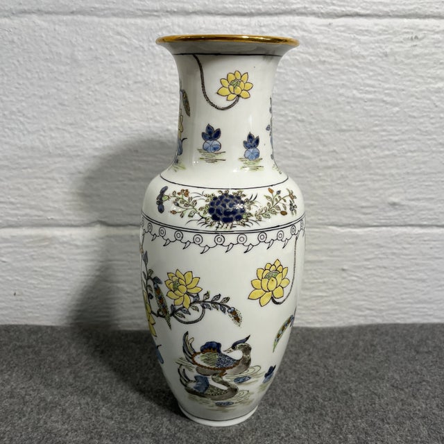 White vase with ducks and garden scenes in tones of blue, yellow, and gold. Accented with a gold rim. Decorated in Hong Kong.