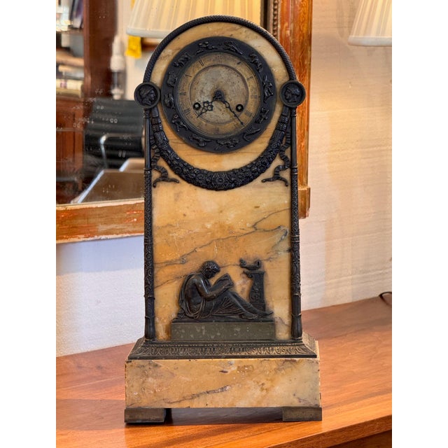 19th century French mantel clock in an arched case of warm yellow veined marble with dark patinated mounts. A scaled band...