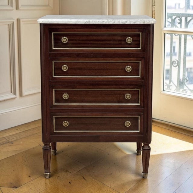French Louis XVI Petite Mahogany Commode with Carrara Marble is beautifully tailored, finished in rich mahogany and topped...