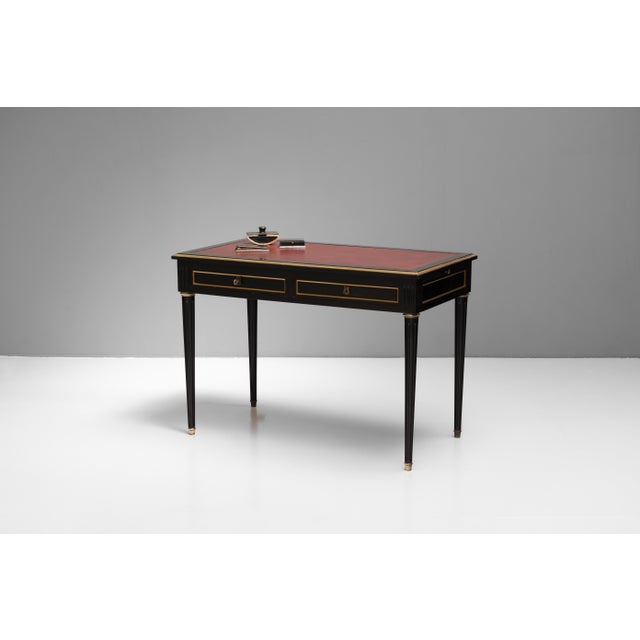 Two drawer writing table in walnut with brass mouldings and original ebonised finish. Circa 1940.