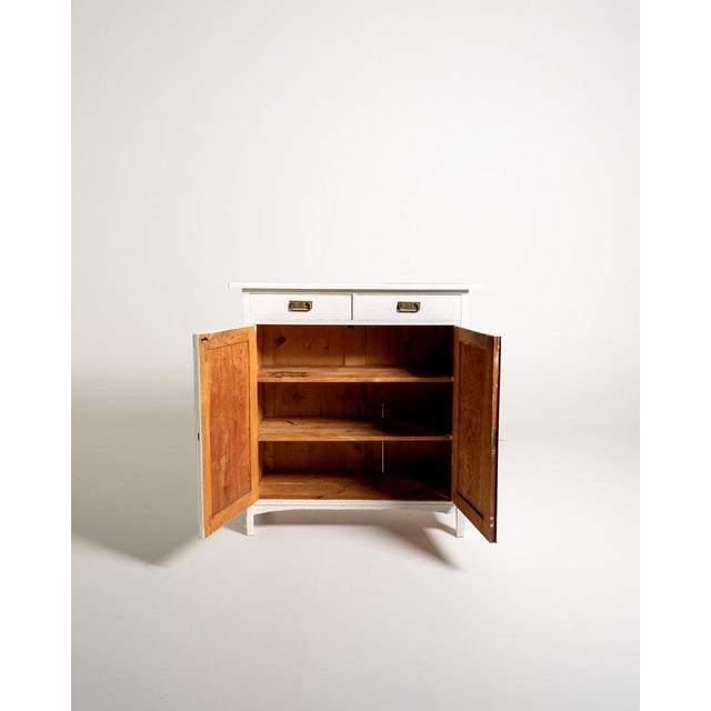 Original Scandinavian vintage sideboard with two hinged doors and two drawers. The white painted wood and the golden metal...
