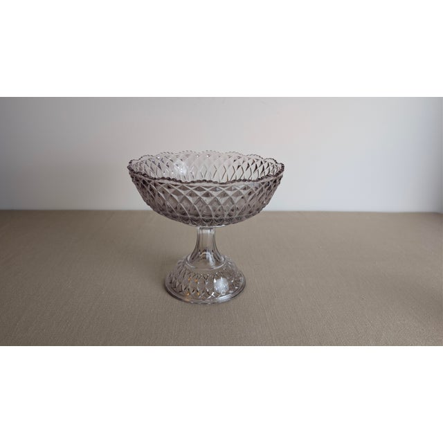 A charming vintage pressed glass compote bowl featuring an elegant pedestal base and a scalloped rim. The bowl showcases...
