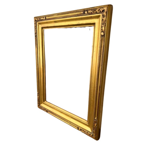 A refined gilt wooden picture frame featuring a broad, beveled profile accented with delicate Art Nouveau-inspired...