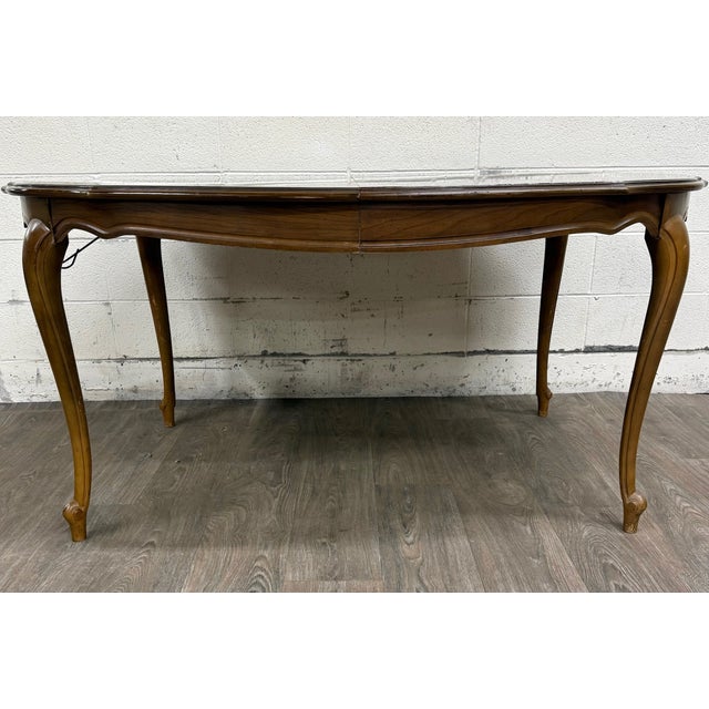 This is a vintage French Provincial–style dining table featuring a shaped walnut-veneer top, scalloped apron, slender...