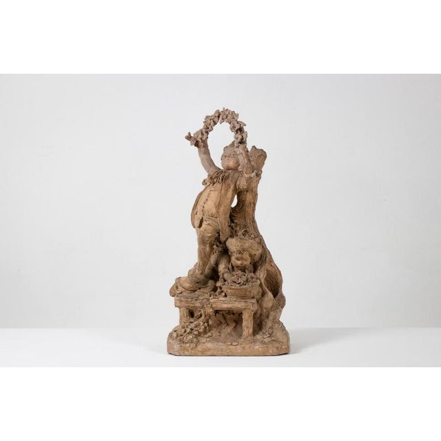 A Rocaille-style terracotta sculpture depicting two children, one arranging a basket of flowers and the other holding a...