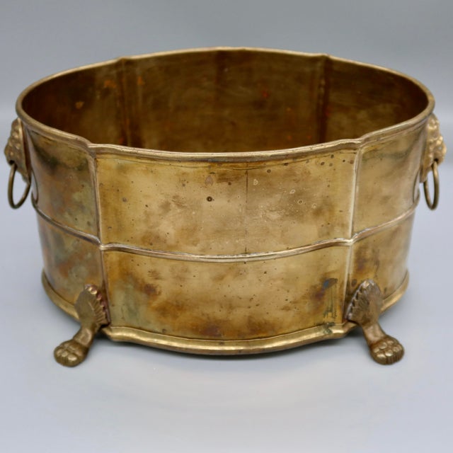 A handsome vintage brass jardinière in the English Regency style, featuring lion-head ring handles on either side and paw-...