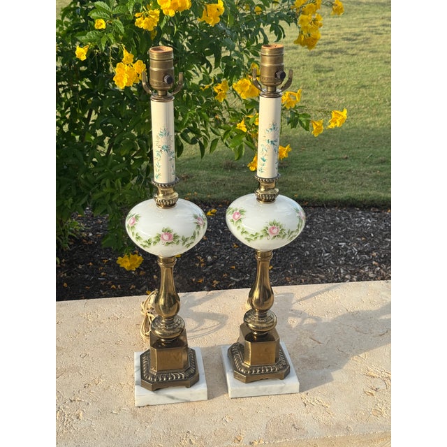 Pair of vintage milk glass and brass lamps on marble bases. The lamps feature a hand-painted floral design on the central...