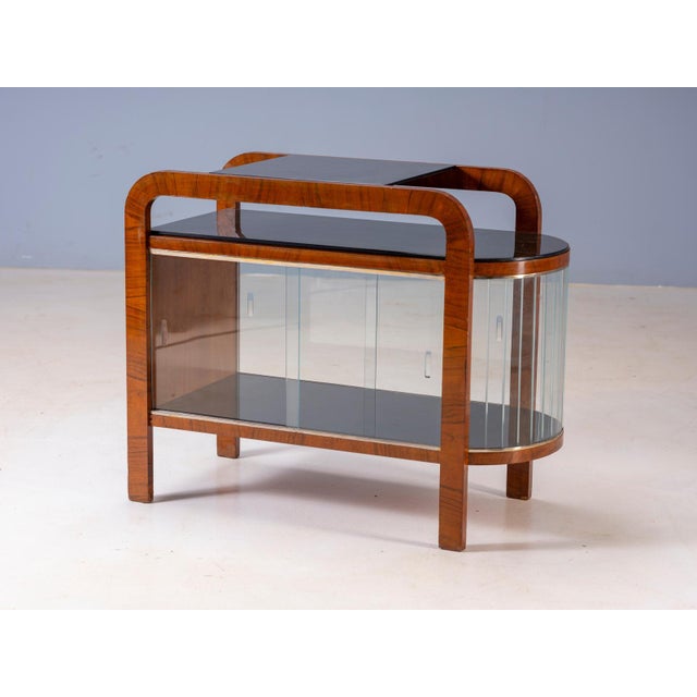 Elegant vintage display cabinet featuring a distinctive curved wooden frame, rounded side section, glass doors, and dark...