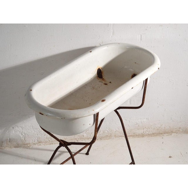 This antique bathtub in enamelled iron rests on a folding stand of bent iron tube. Originates from Central Europe, from...