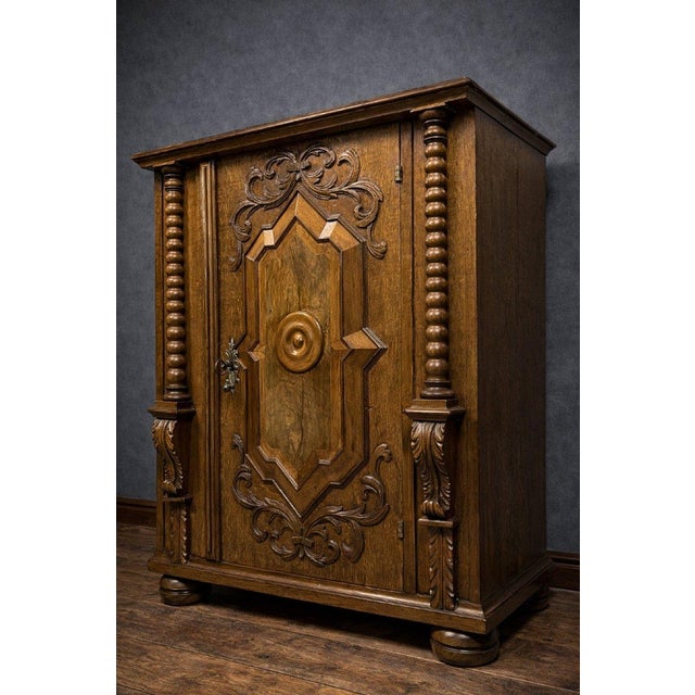 A richly carved, solid wood display cabinet dating from the 17th century. the front is adorned with a central molded and...