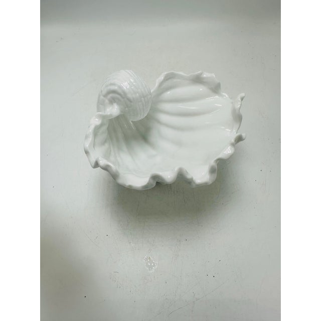 This is a white ceramic shell-form planter or cachepot. Appearance • Sculpted to resemble a large ocean conch or murex...