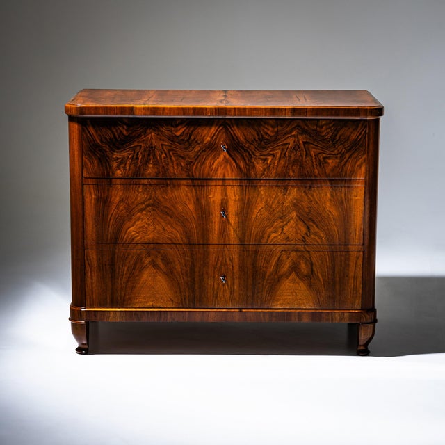 Biedermeier chest of drawers with three drawers and rounded corners. The piece is veneered in walnut and has been hand-...
