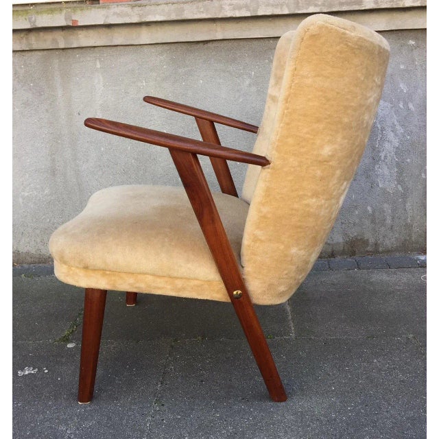 This low-seated Danish armchair with a solid teak frame features organically shaped armrests, large brass assembly screws...
