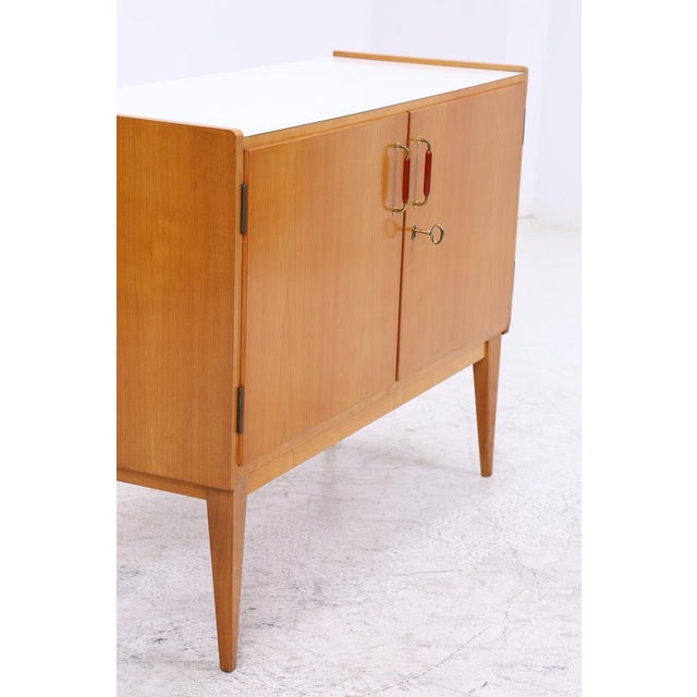 Vintage 1960s chest of drawers with a light wood finish, slender tapered legs, and original handles. Behind the lockable...