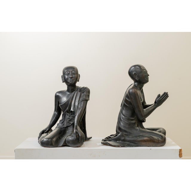 A pair of freestanding sculptures depicting two Buddhist monks in an attitude of devotion and respect, wearing traditional...