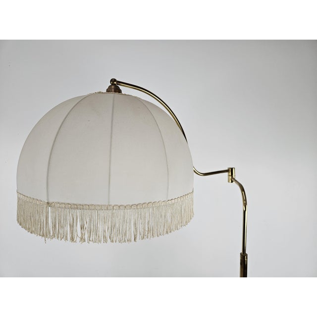 Golden metal floor lamp with arm adjustable in width and depth, perfect for use as a reading lamp in a living room or...