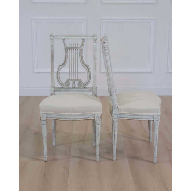 A beautiful pair of antique French neoclassical chairs featuring elegant lyre-form backs and their original painted...
