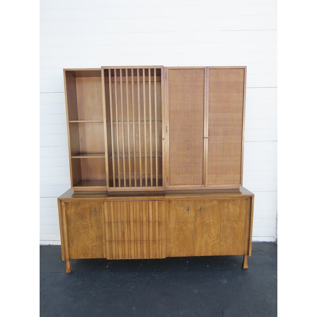 This Stunning Cabinet is made of wood, walnut, veneer, and metal. The piece was made by John Widdicomb, and it is stamped....