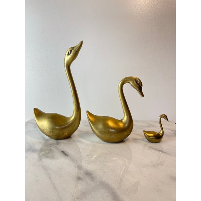 Set of three vintage brass swan figurines featuring elegant, sculptural forms and a warm golden patina. Each swan is...