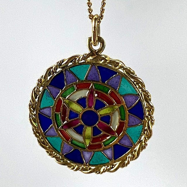 An 18 karat (18K) yellow gold charm pendant designed as a round medal with a rope-twist edge depicting a stained glass...