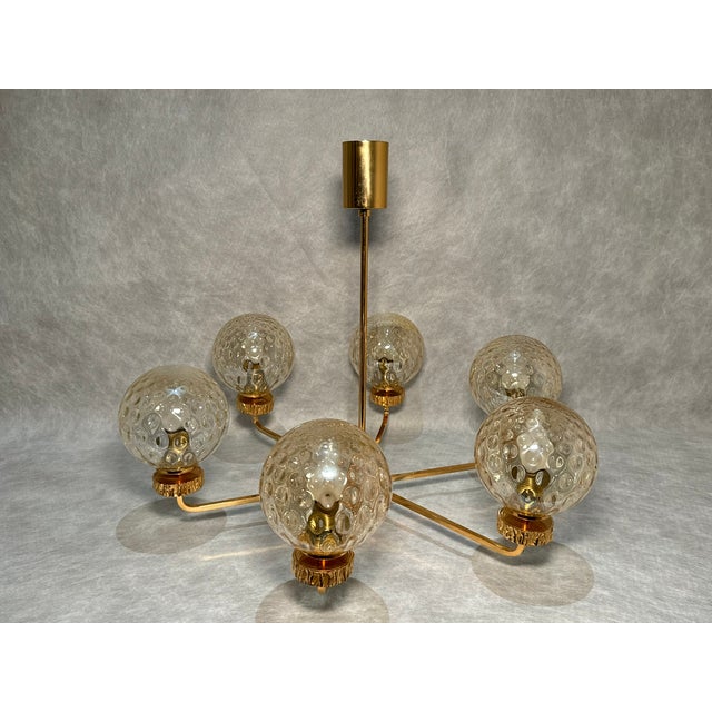 A striking Italian chandelier from the 1970s featuring a gold-toned metal frame and six deep, textured glass bowls. The...