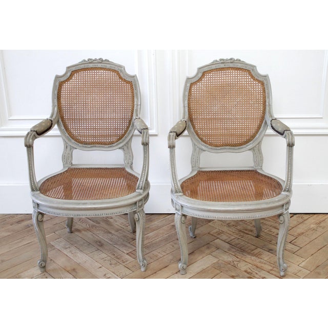 19th century painted and carved ribbon cane back open armchairs painted in a soft pale Swedish gray color, with natural...