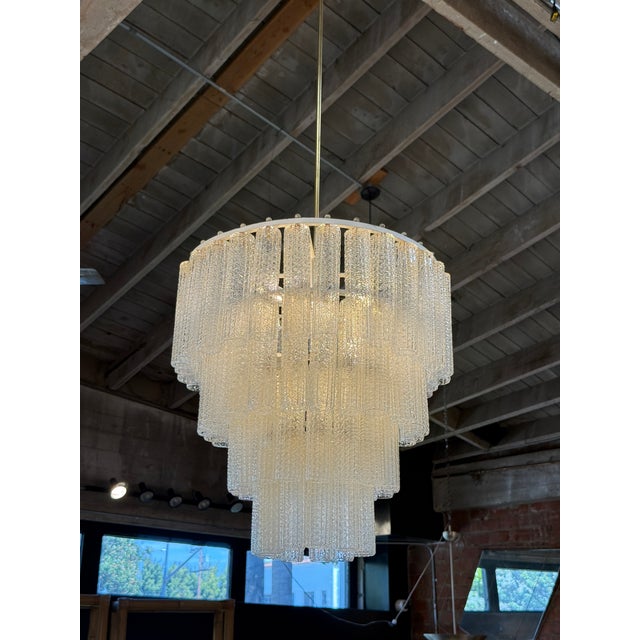 Elegant Italian chandelier featuring four cascading tiers of textured glass panels supported by a brass frame. The...