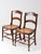 A handsome pair of early 20th-century ladderback dining chairs featuring hand-caned seats, turned front legs, and turned...